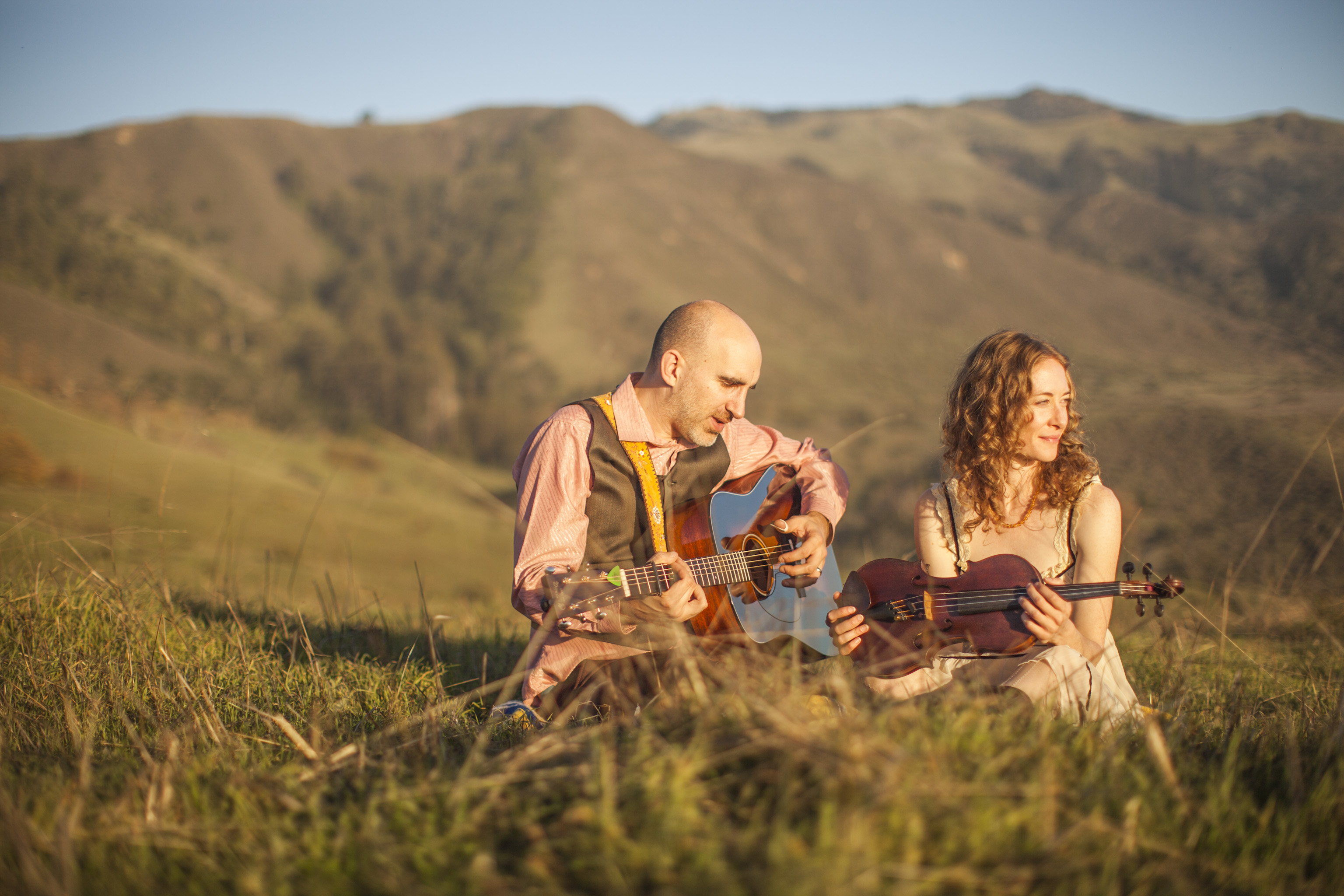 Dan Frechette & Laurel Thomsen posing with their violin and guitar in a field