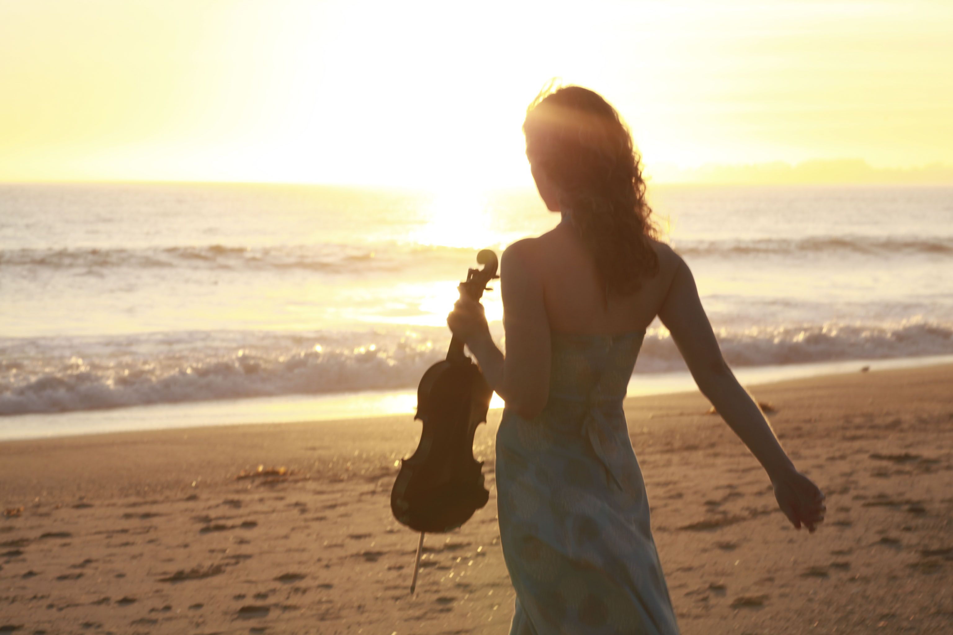 Violinist Laurel Thomsen holding her violin at the beach at sunset